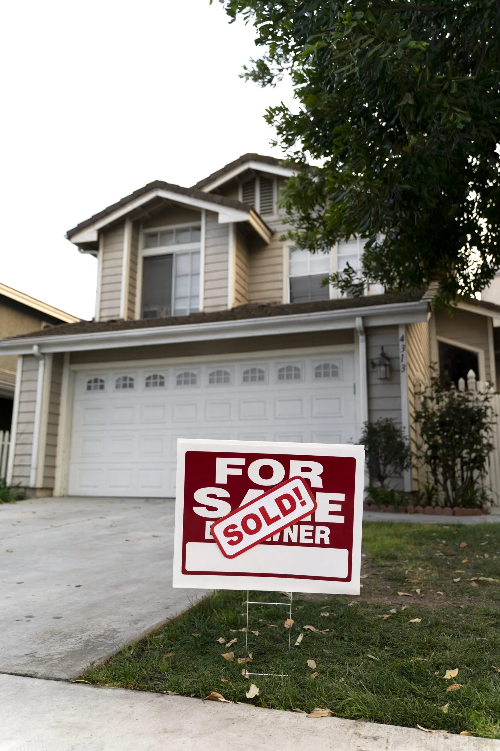 A house with a "For Sale by Owner" sign in front now marked "Sold" in red letters. The image captures the conclusion of a real estate sale in a residential neighborhood.